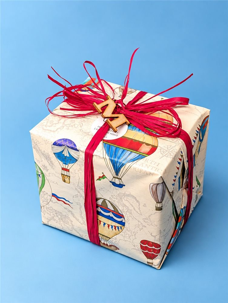Regalo incartato a mano con carta delle mongolfiere, rafia rossa e iniziale in legno